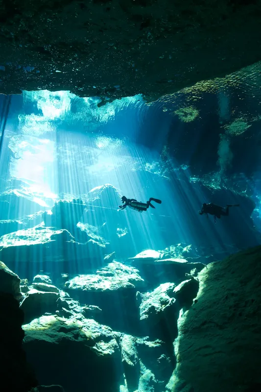 Deux plongeurs explorent une grotte sous-marine éclairée par le soleil