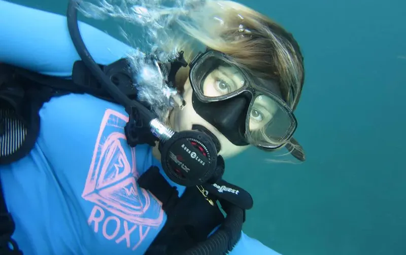 Plongeuse souriante avec masque et détendeur sous l'eau turquoise