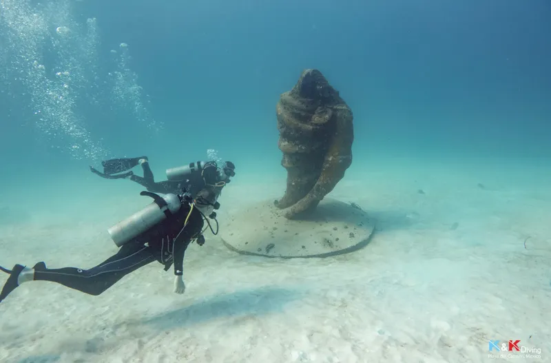 Plongeur explorant une sculpture sous-marine dans une eau turquoise claire