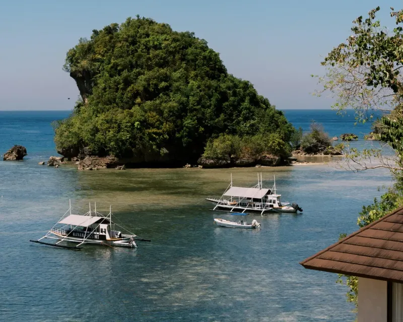 Île tropicale verdoyante avec des bateaux de pêche dans l'eau turquoise