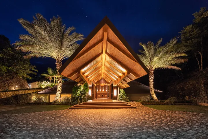Entrée illuminée d'un bâtiment avec toiture en bois et palmiers