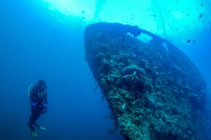 Plongeur explorant l'épave d'un grand navire sous l'eau bleue