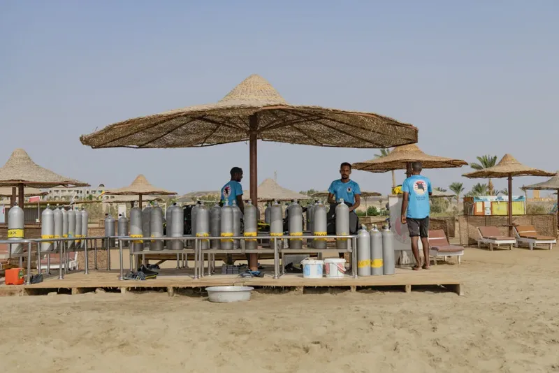 Trois personnes près de nombreuses bouteilles de plongée sous des parasols