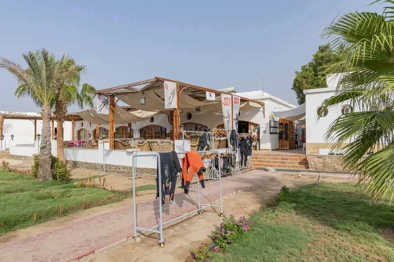 Terrasse ombragée d'un centre de plongée avec combinaisons et enseignes
