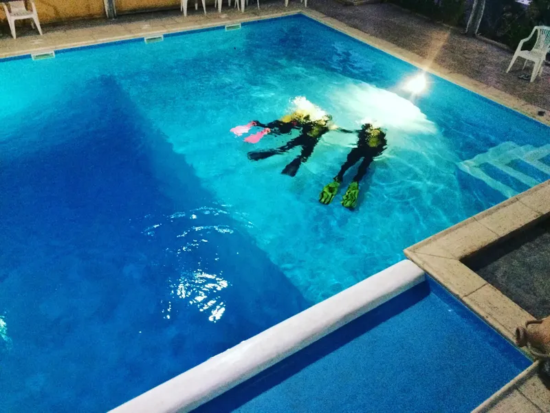 Deux plongeurs s'entrainent dans une piscine, équipés de palmes et bouteilles
