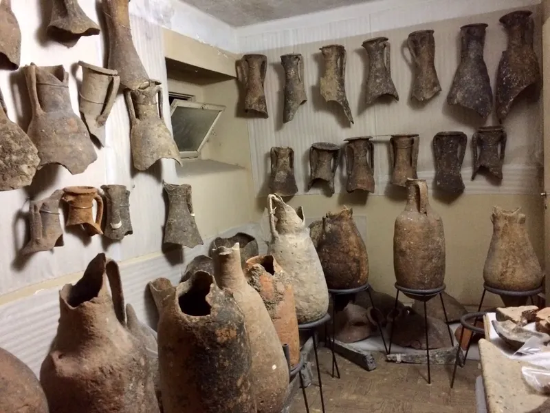 Amphores anciennes et fragments de poterie exposés dans une pièce sombre