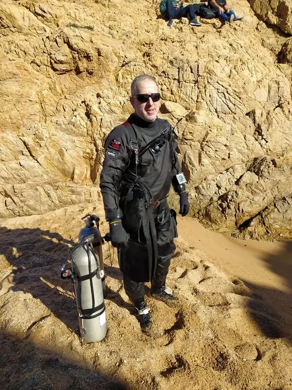 Plongeur en combinaison noire avec bouteille sur un terrain rocheux
