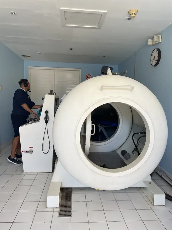 Un homme manipule les commandes d'une chambre de recompression blanche