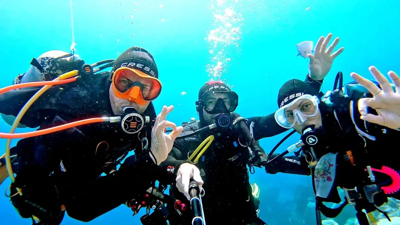 Trois plongeurs souriants font des signes de la main sous l'eau