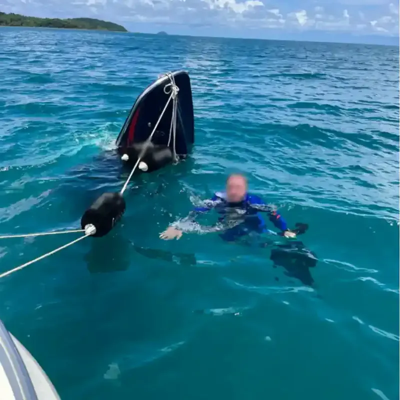 Plongeur en combinaison nageant près d'un bateau et d'un flotteur noir