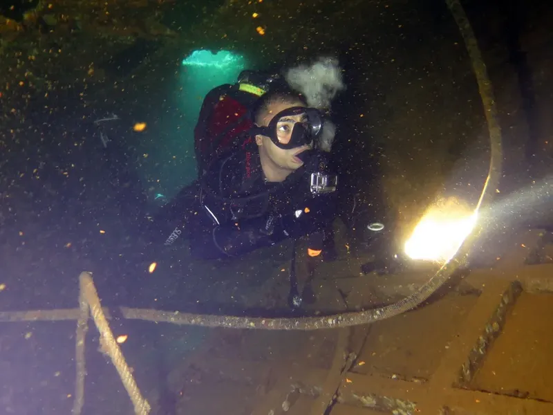 Plongeur avec masque et détendeur explore un épave sous-marin sombre