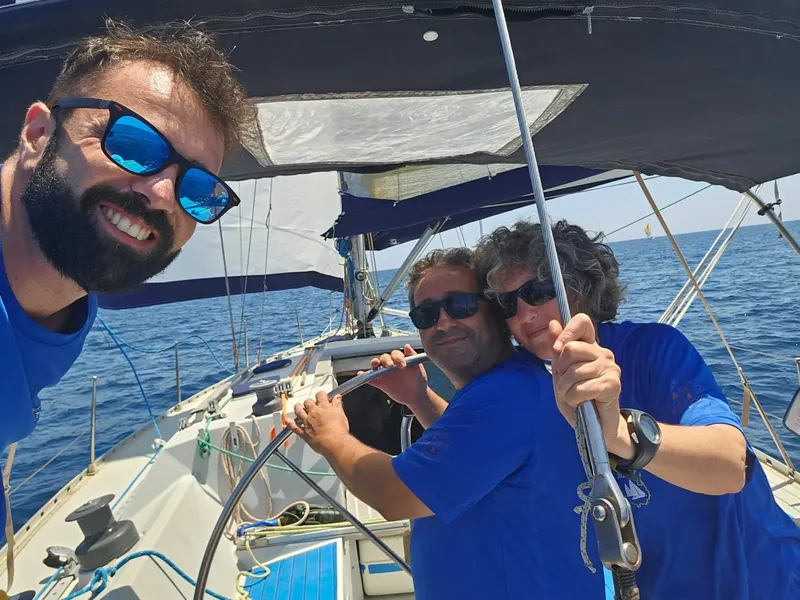 Trois hommes souriants sur un voilier en pleine mer ensoleillée
