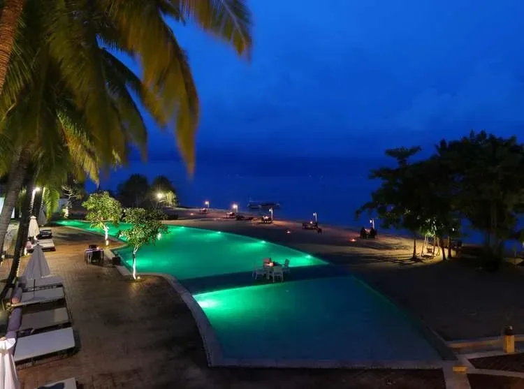 Vue nocturne d'une piscine illuminée face à la mer et bateaux