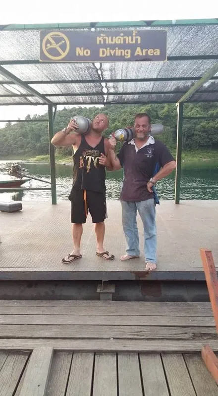 Deux hommes souriants tenant des bouteilles de plongée sur un ponton