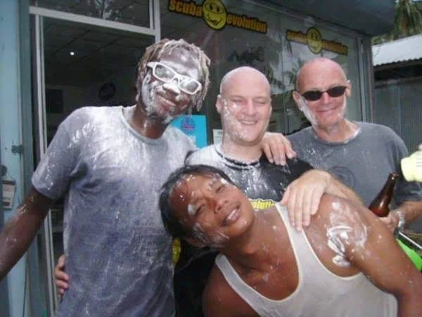 Quatre personnes sourient, couvertes de mousse blanche, devant un local