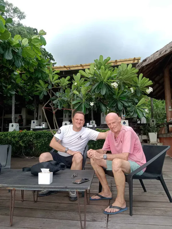 Deux hommes souriants assis à une table en extérieur, ambiance détendue