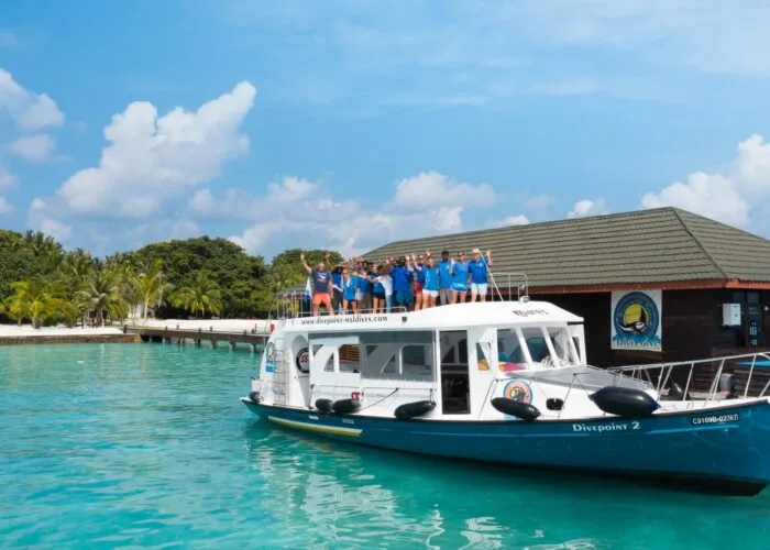 Groupe de plongeurs souriants sur un bateau devant un bâtiment tropical