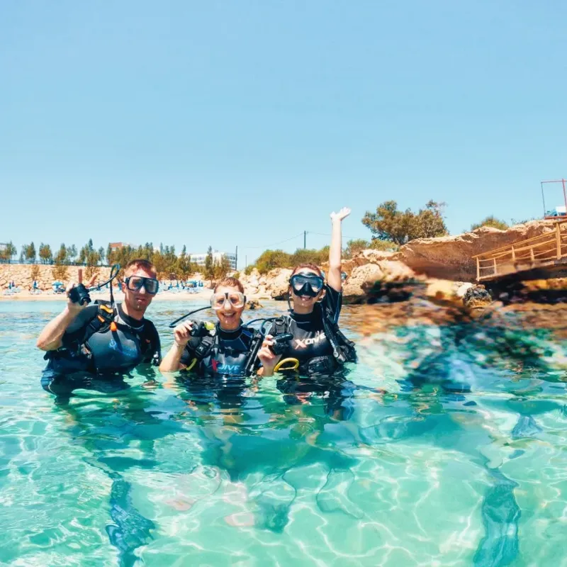 Trois plongeurs souriants en combinaison dans une eau turquoise claire