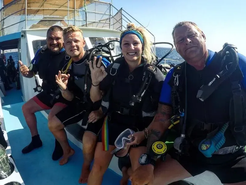 Groupe de plongeurs souriants sur un bateau, équipement complet visible