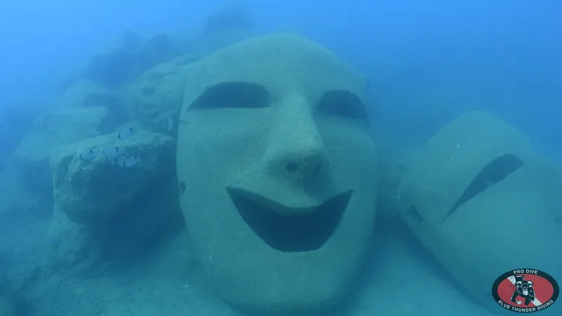 Sculpture sous-marine d'un visage souriant, colonisée par la vie marine