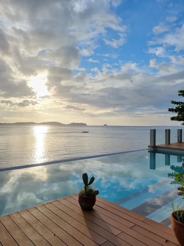 Vue sur la mer, piscine à débordement, bateau au loin, ciel nuageux