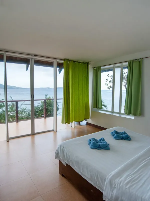 Chambre avec vue sur mer, rideaux verts, literie blanche et décorée