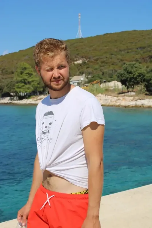 Un jeune homme souriant, torse nu, sur un ponton ensoleillé