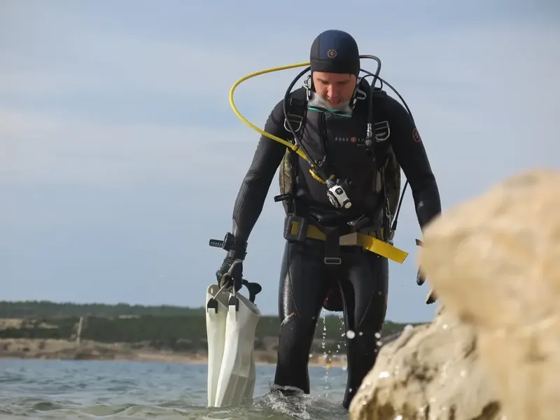 Plongeur en combinaison sortant de l'eau avec palmes à la main