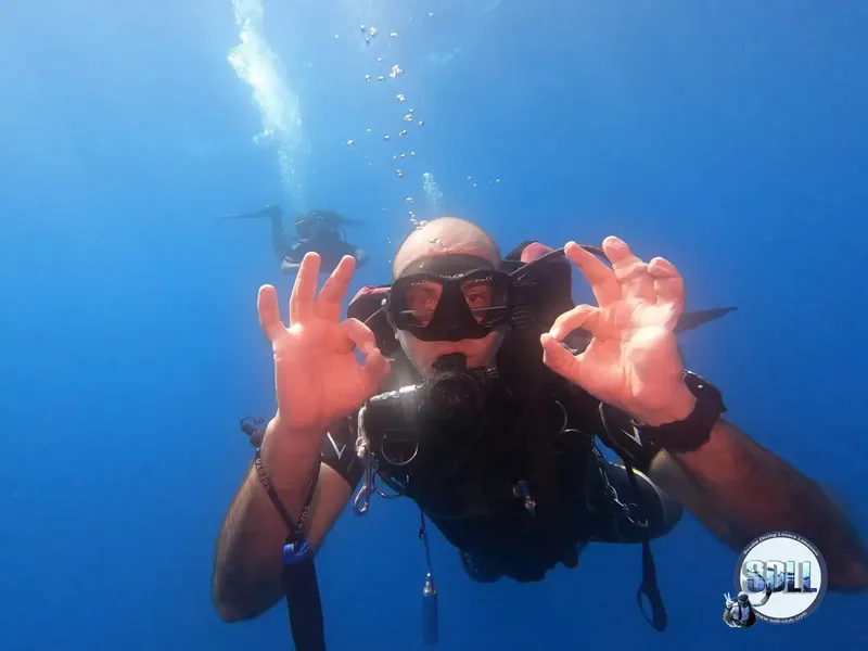Plongeur souriant sous l'eau, faisant le signe OK avec ses mains