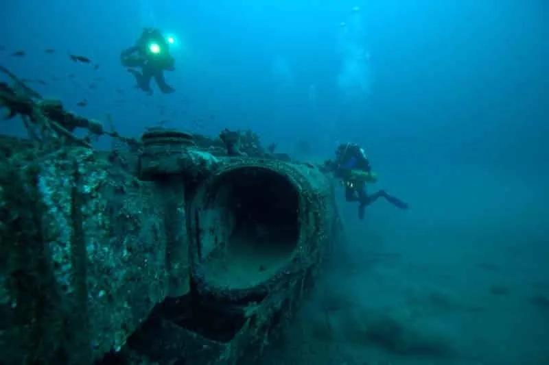 Deux plongeurs explorent une épave sous-marine bleu turquoise