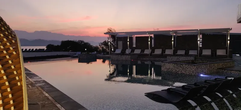 Piscine avec transats, bâtiments et ciel coloré au coucher du soleil