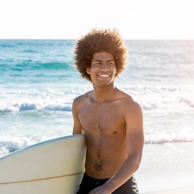 Jeune homme souriant tenant une planche de surf sur la plage
