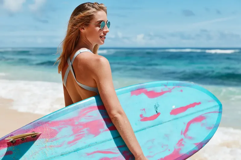 Jeune femme souriante portant des lunettes de soleil avec une planche de surf