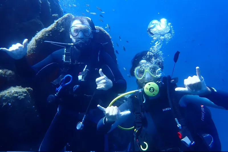 Deux plongeurs souriants font des signes de la main sous l'eau