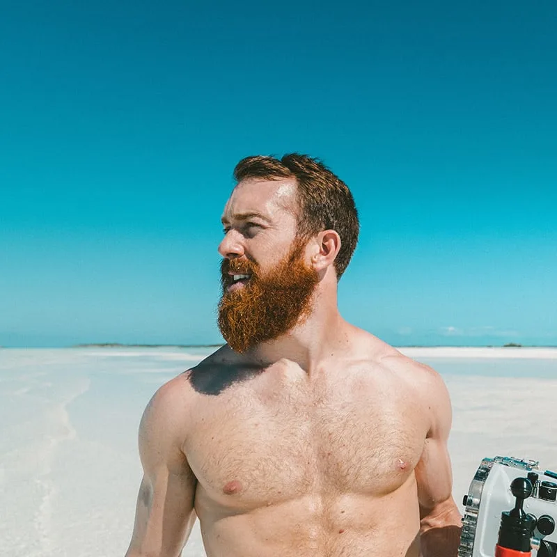 Homme barbu souriant sur une plage paradisiaque ensoleillée