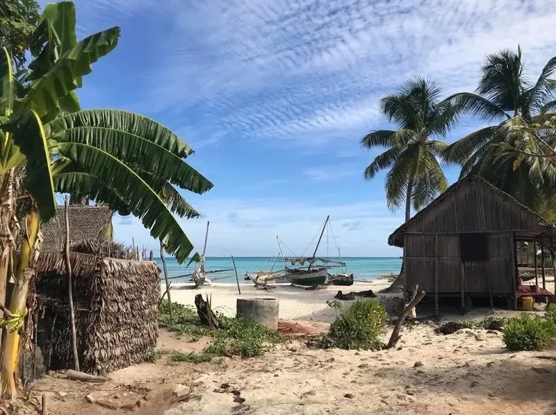 Plage de sable blanc avec quelques bateaux et bâtiments traditionnels