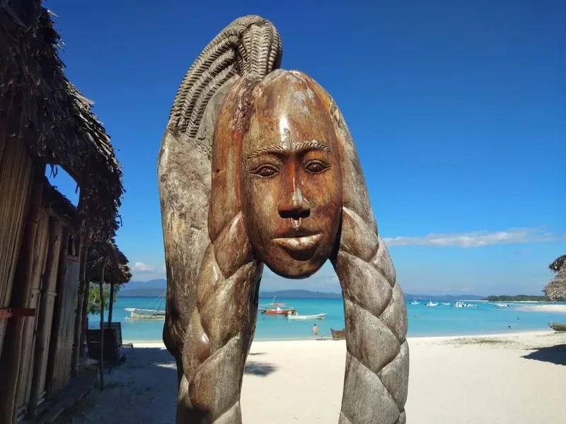 Sculpture en bois d'un visage, plage de sable blanc et mer turquoise