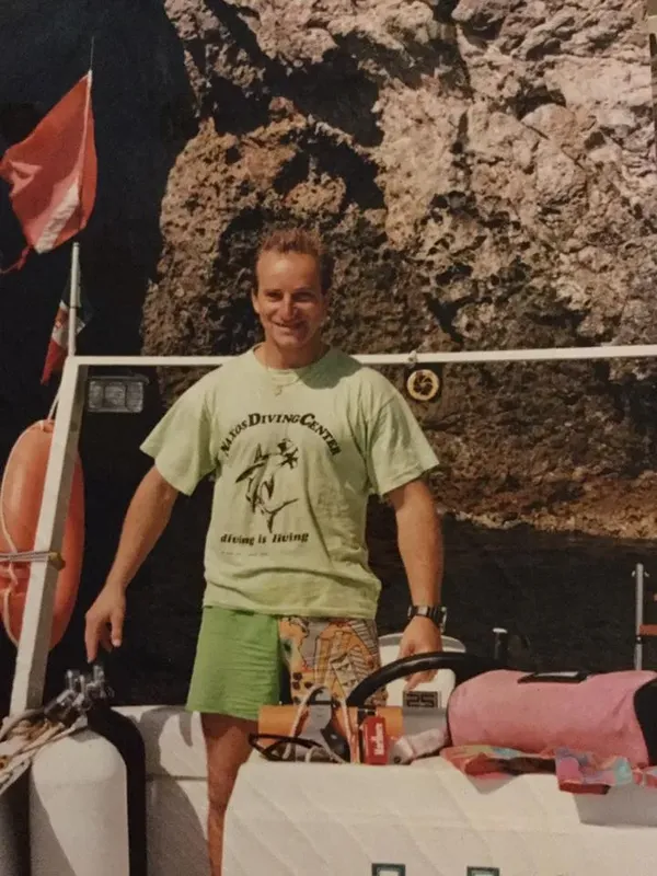 Homme souriant sur un bateau, portant un t-shirt de centre de plongée