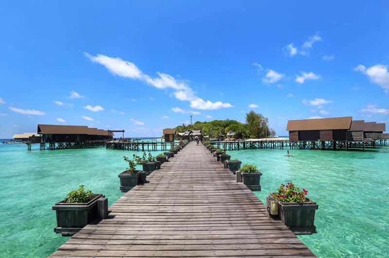 Long ponton en bois menant à des bungalows sur pilotis turquoise