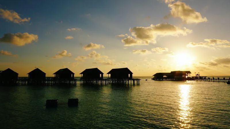 Coucher de soleil sur l'océan avec des bungalows sur pilotis et des personnes