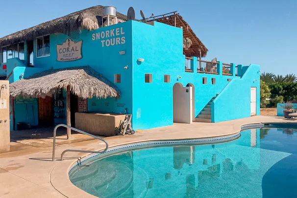 Bâtiment bleu turquoise avec piscine au premier plan et végétation