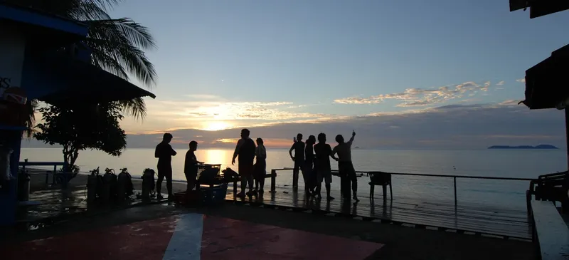 Groupe de personnes sur un ponton au coucher du soleil en bord de mer
