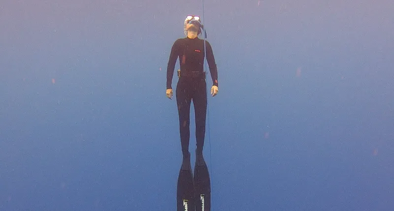 Plongeur en combinaison noire, flottant verticalement dans l'eau bleue