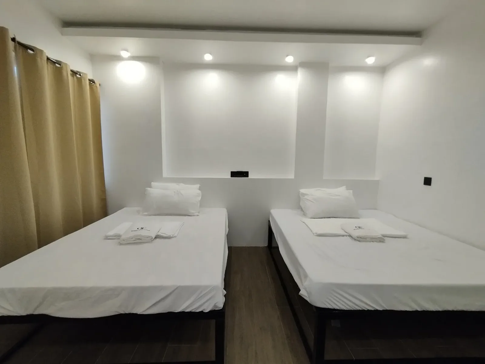 Chambre avec deux lits simples, draps blancs, rideaux beiges et éclairage