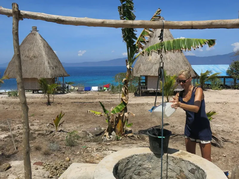 Femme remplissant un seau d'eau près de huttes sur une plage