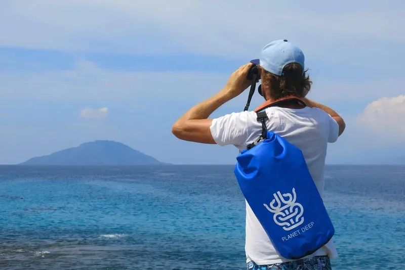 Homme observe l'horizon avec des jumelles sac étanche bleu