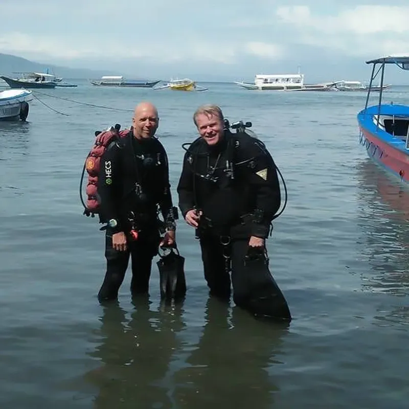 Deux plongeurs en combinaison, équipés, souriants dans l'eau peu profonde