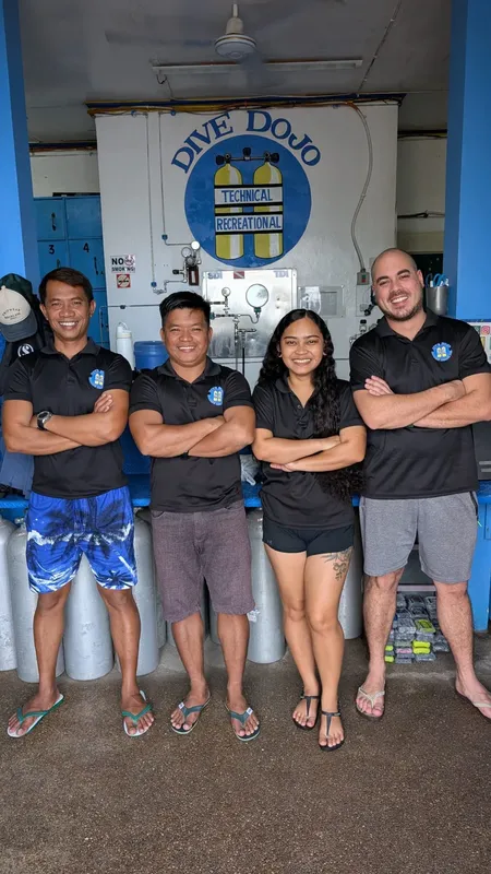 Quatre personnes souriantes posent devant des bouteilles et un logo de plongée