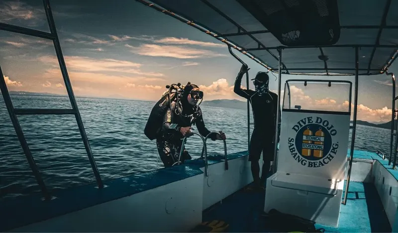 Deux plongeurs se préparent à bord d'un bateau de plongée au coucher du soleil