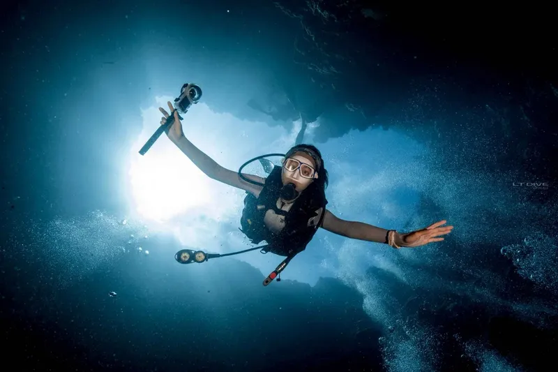 Plongeuse souriante, bras ouverts, évolue dans une eau bleue lumineuse
